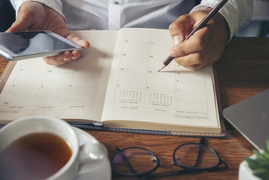 computer, hand writing in calendar, cup of coffee